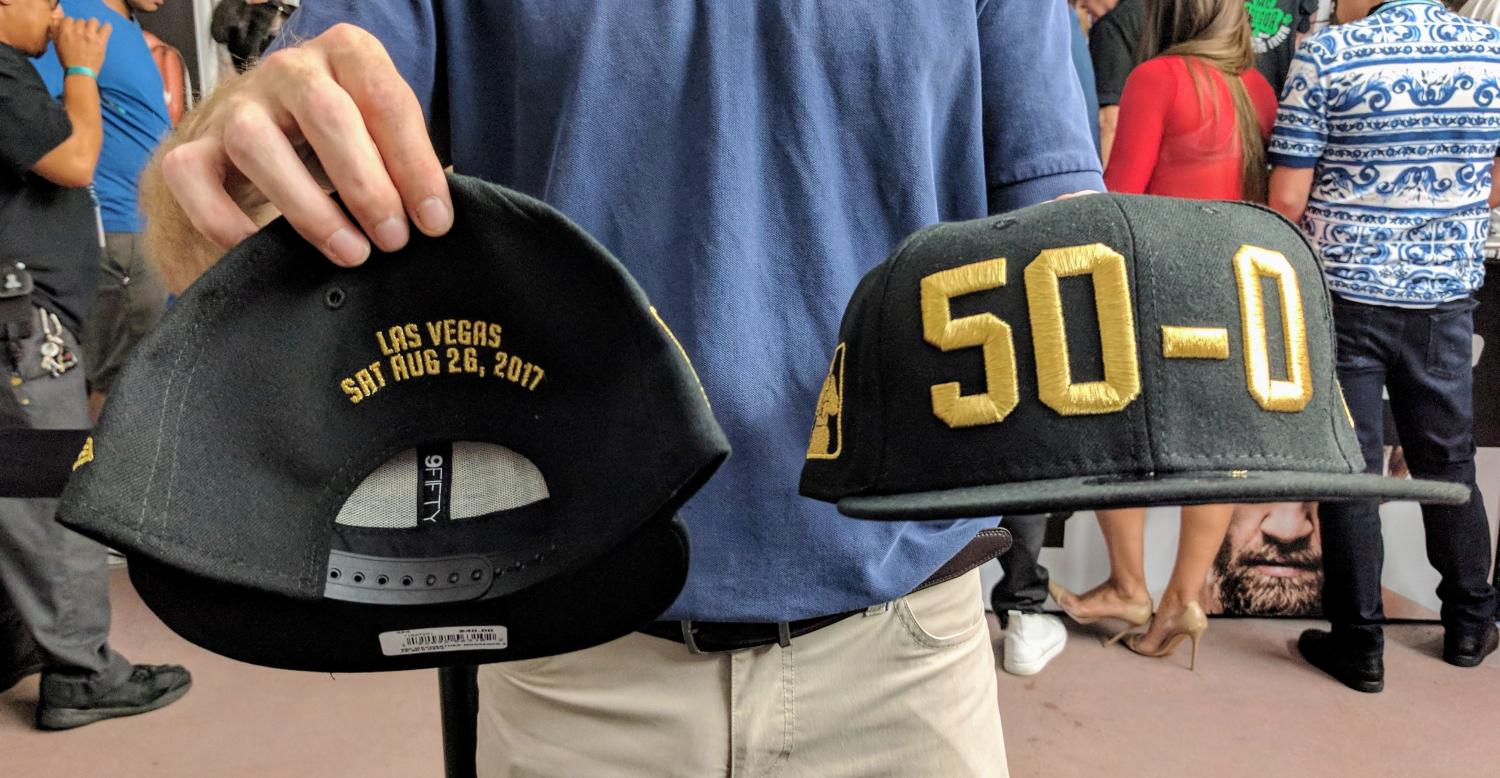 A man holds up the front and back of a baseball cap that mark Floyd Mayweather's record of 50-0